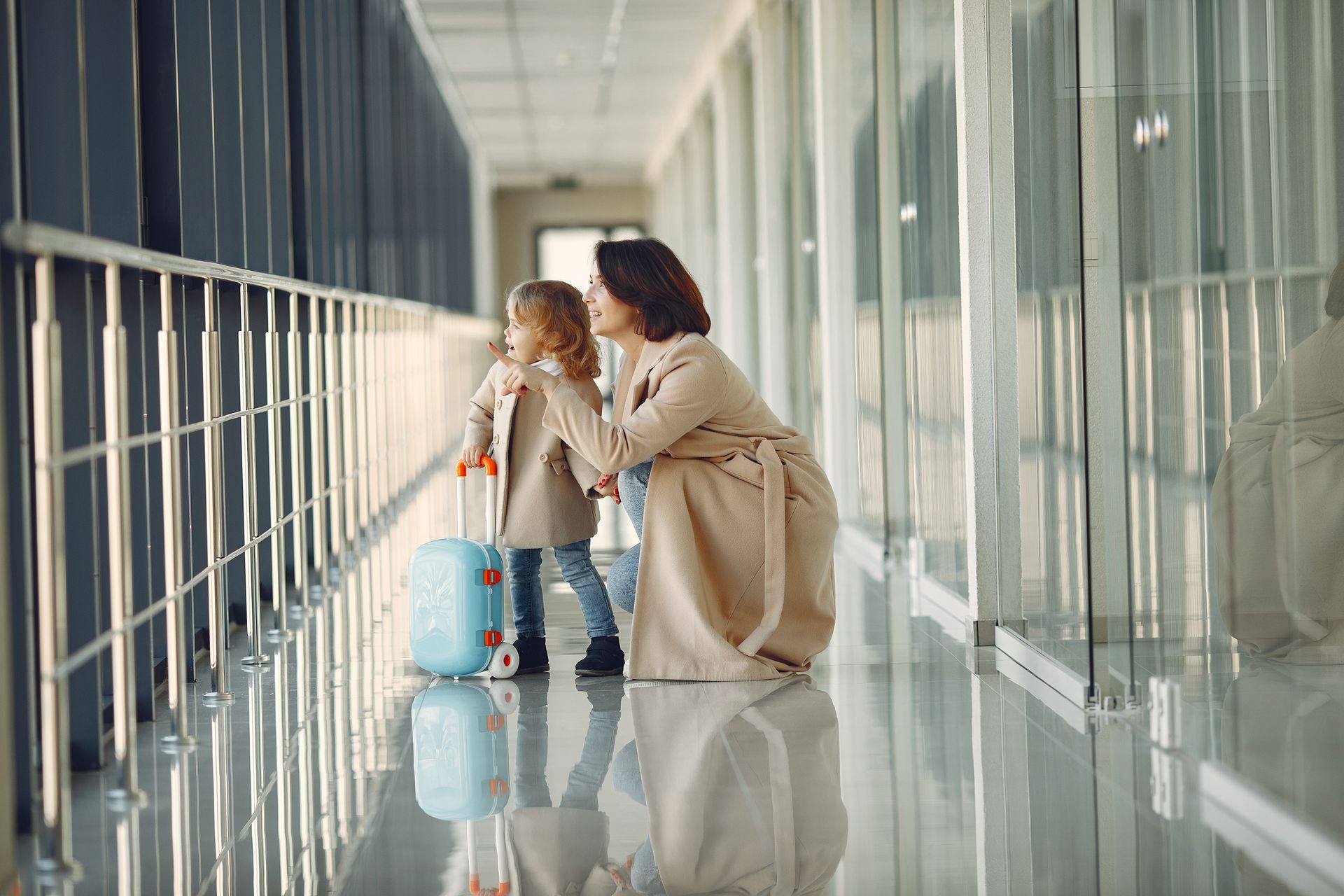 Mama z córeczką i małą walizką patrzą przez okno na lotnisku